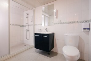 Un baño con ducha de vidrio, un inodoro blanco y un gabinete negro con un espejo arriba.