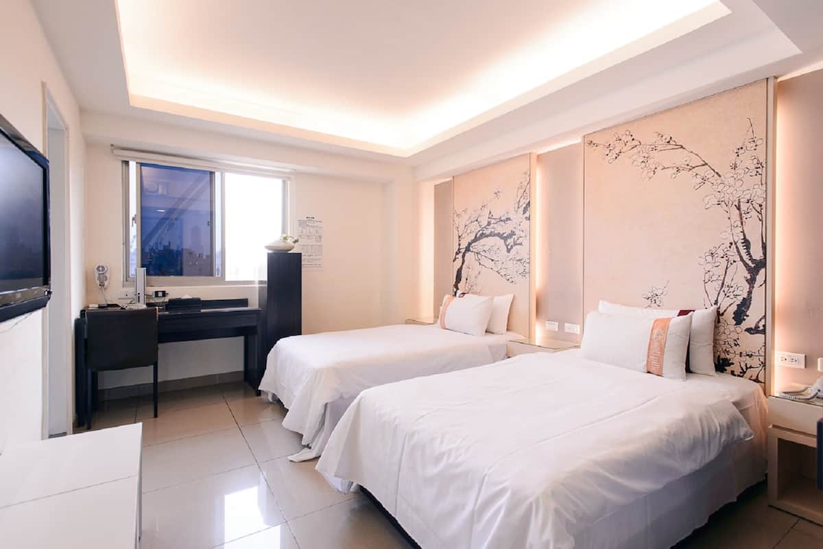 Ein Hotelzimmer mit zwei Einzelbetten, einem Schreibtisch mit Stuhl, einem Flachbildfernseher, einem Fenster und einer Wand mit floralem Wandbild.