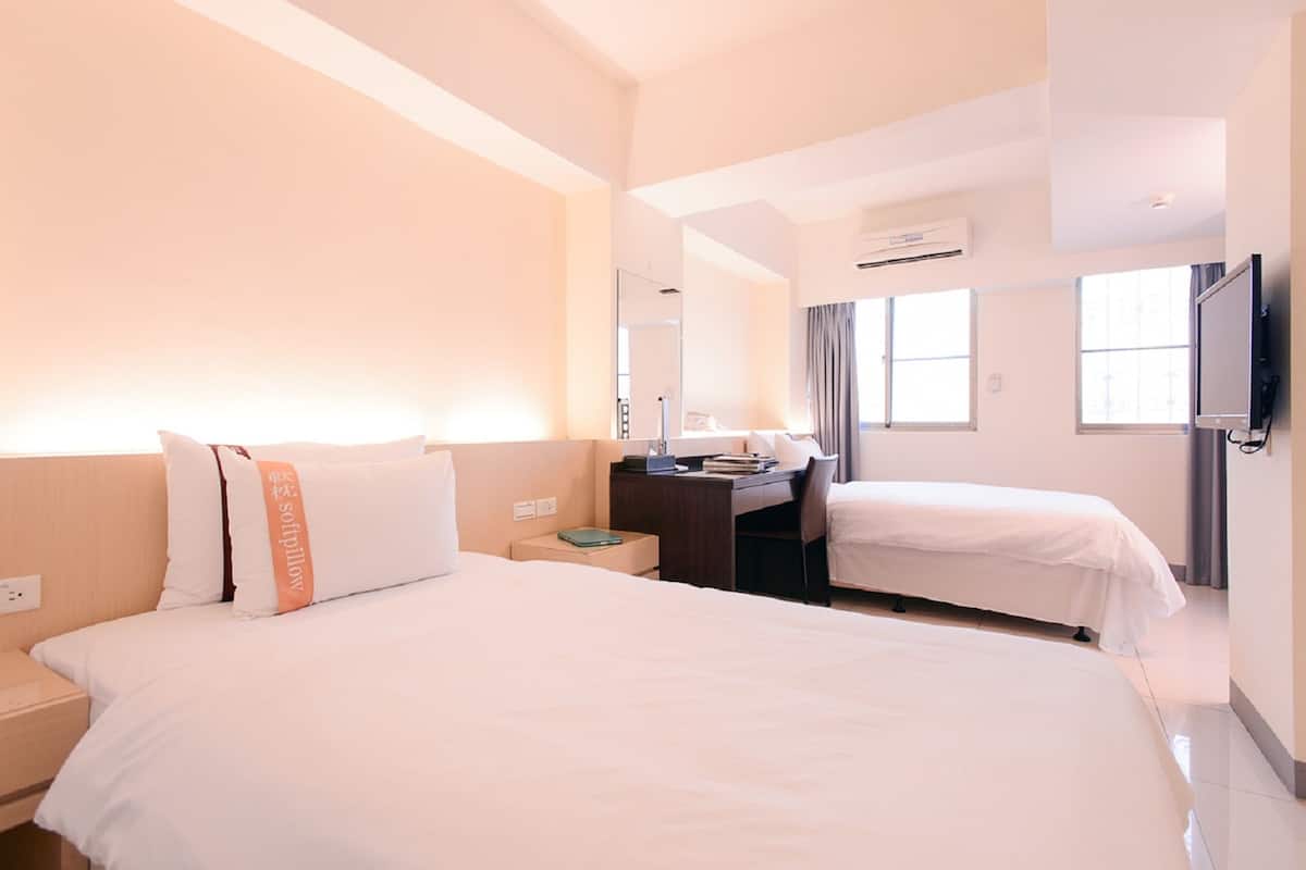 Ein Hotelzimmer mit zwei Betten, einem Schreibtisch, einem Stuhl, einem Fernseher und einem Fenster.