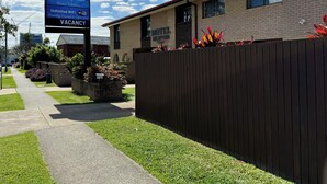 A motel with a signboard listing amenities like comfortable beds, reverse cycle air conditioning, large smart TVs, pet-friendly rooms, and a guest kitchen. - Toreador Motel (Coffs Harbour)
