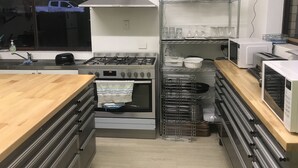 A kitchen with a gas stove, oven, and stainless steel appliances. There are shelves with glassware and a window with a view of a vehicle outside. - Toreador Motel (Coffs Harbour)
