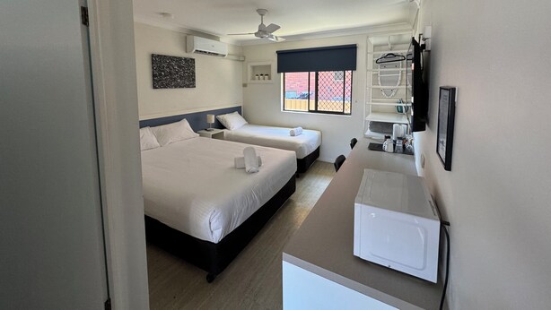 A hotel room with two beds, a ceiling fan, an air conditioning unit, a window with a view, a small table with a kettle, and a microwave. - Toreador Motel (Coffs Harbour)