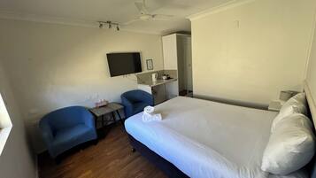 Quarto de hotel com uma cama grande, uma escrivaninha com cadeira, televisão, ventoinha de teto e uma pequena cozinha.