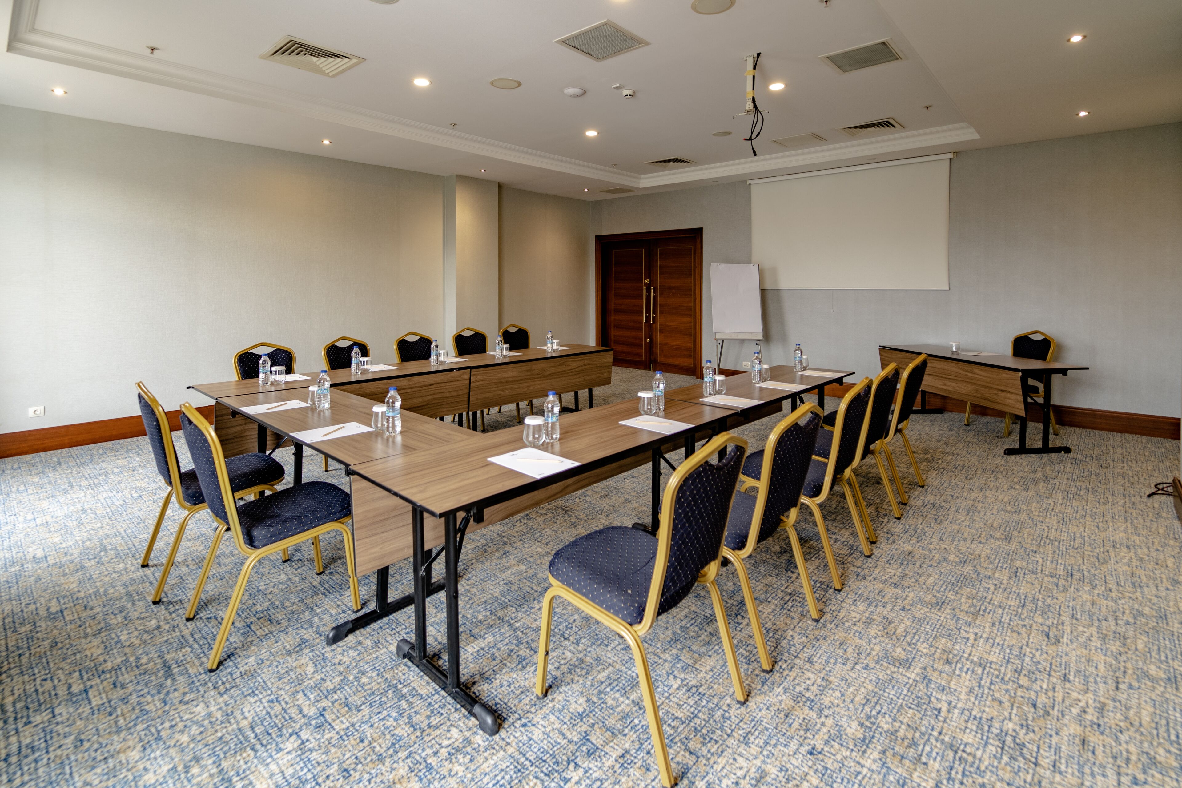 A conference room with a long table, chairs, and a projector screen.