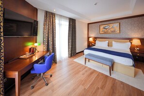 Ett hotellrum med en säng, sänglampor, ett skrivbord med en stol, en tv och mönstrade gardiner.