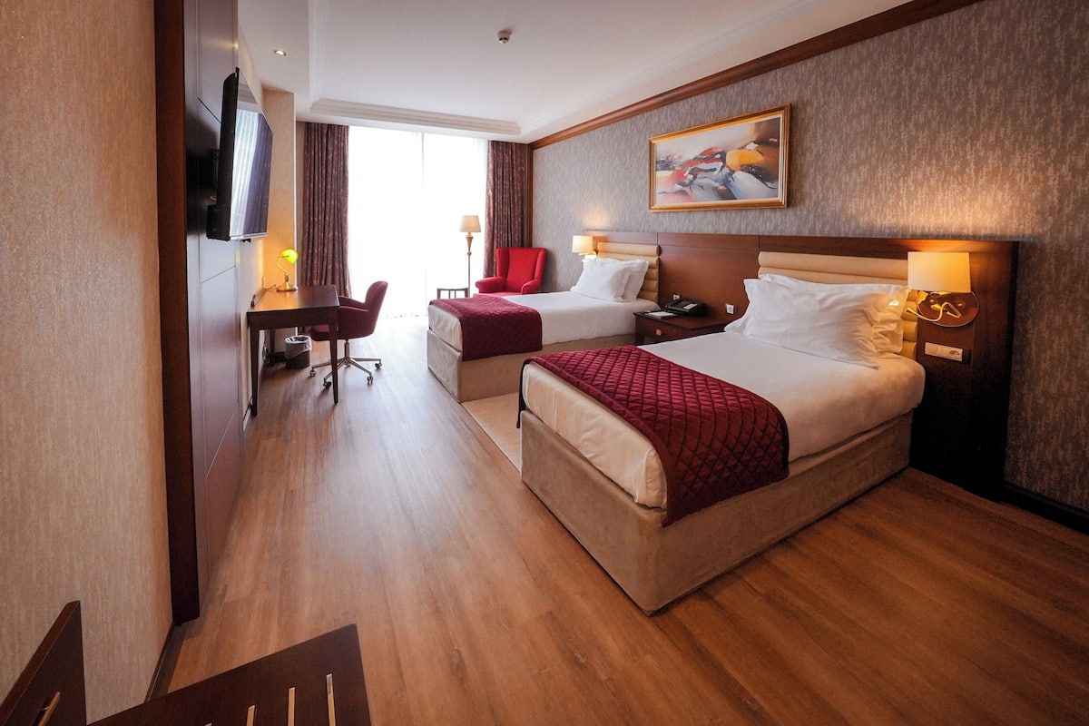 Ein Hotelzimmer mit zwei Betten, einem Schreibtisch, einem Sessel, einem Fernseher und einem Bild an der Wand.