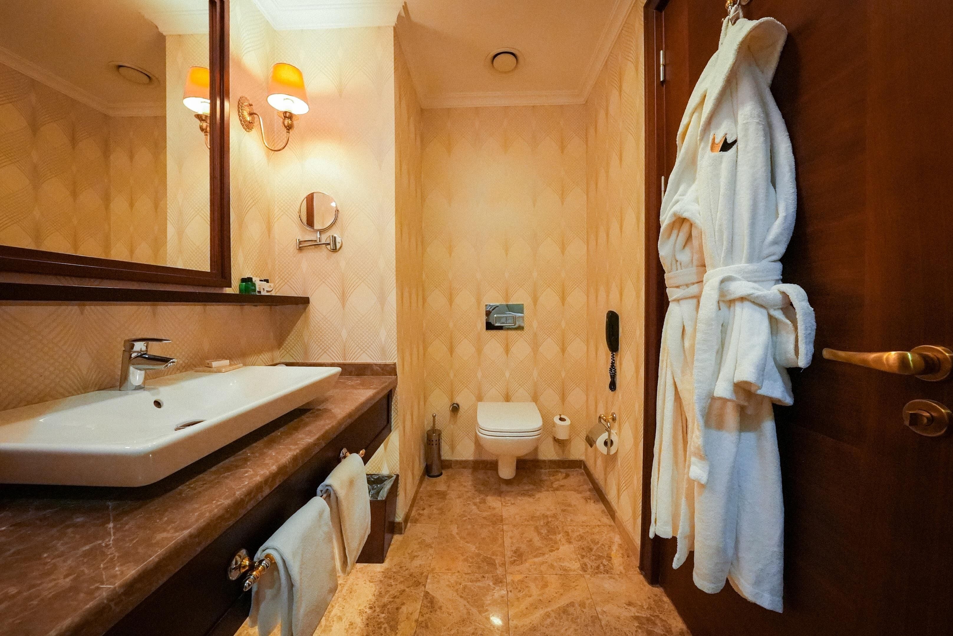 Ein Badezimmer mit Waschbecken, Toilette und einem Bademantel, der an der Tür hängt.