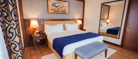 Habitación de hotel con una cama grande, lámparas de noche, una mesita de noche, un espejo y una cortina estampada.