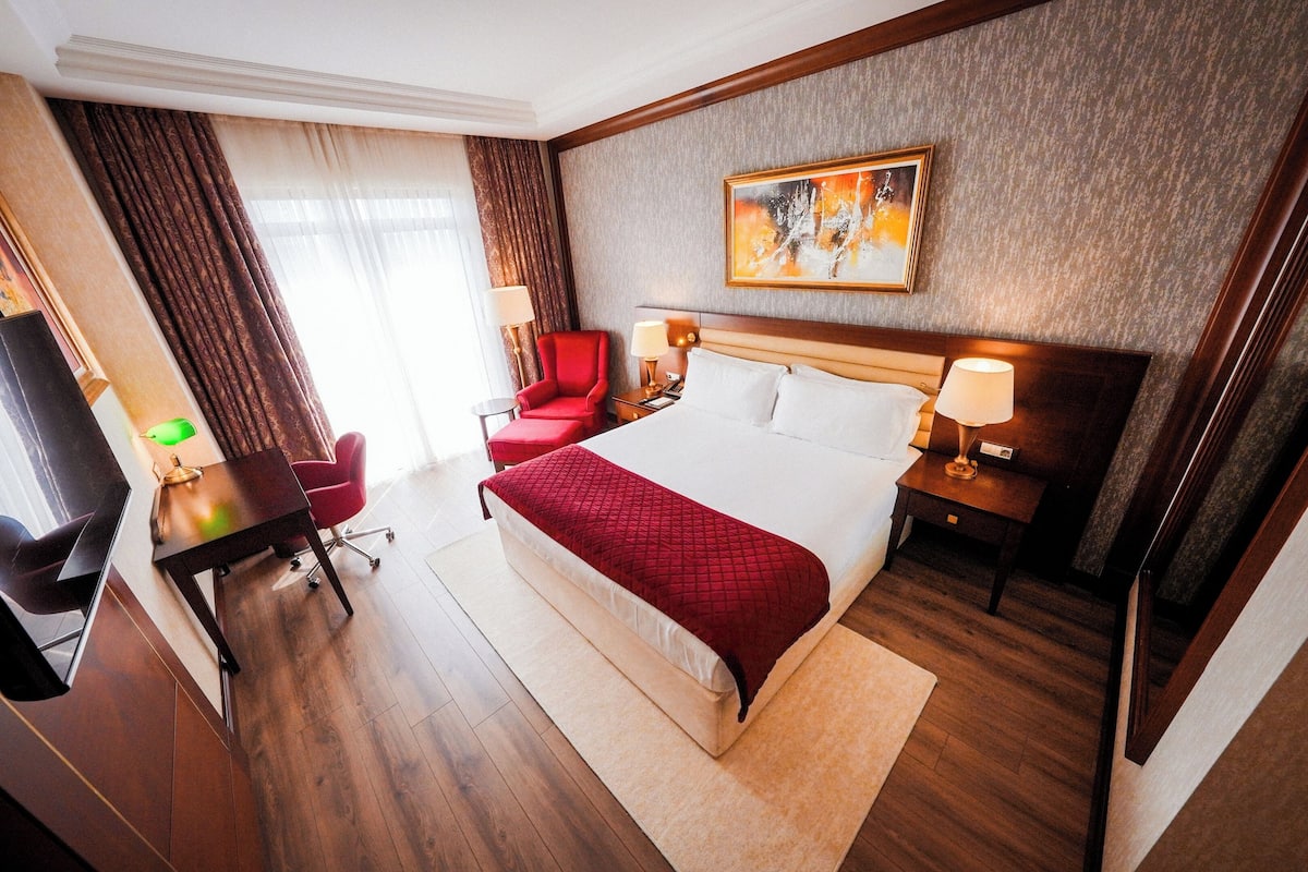 Ein Hotelzimmer mit Bett, Schreibtisch, Stuhl, Fernseher und einem Bild an der Wand.