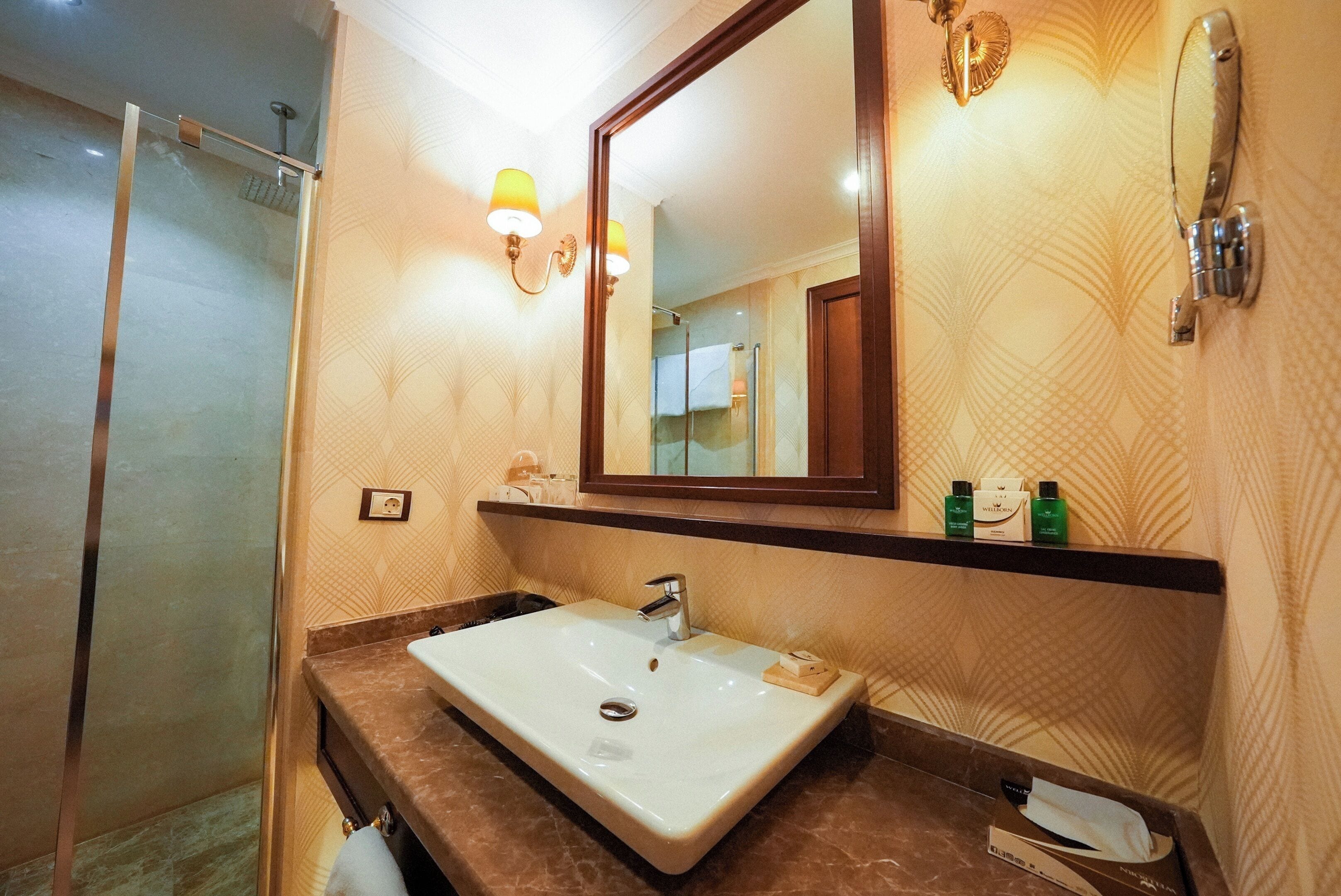 A bathroom with a sink, mirror, shower, and towel rack.