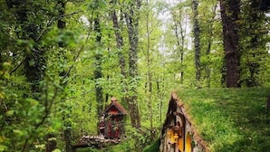 A forest path leading to a rustic house with a thatched roof and a small wooden bridge. - Wellborn Luxury Hotel (Basiskele)