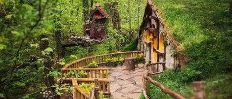 Un sentier forestier menant à une maison rustique avec un toit de chaume et un petit pont en bois.
