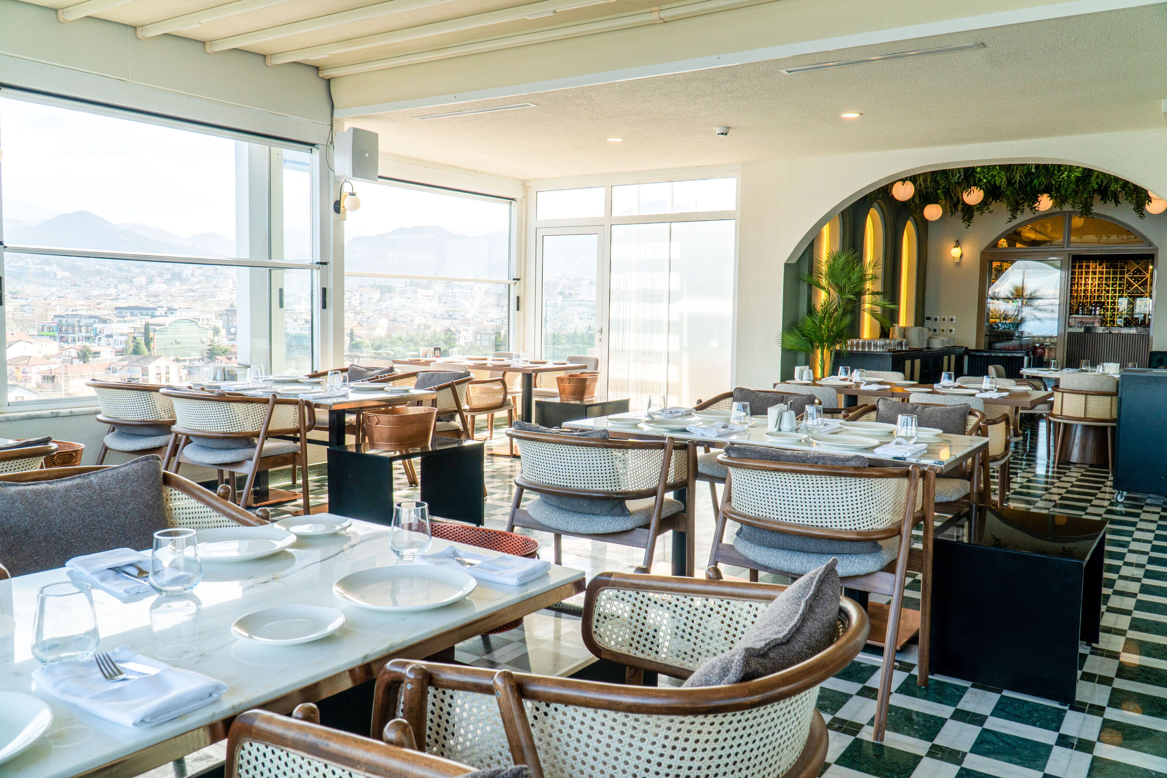 Un restaurante con mesas y sillas altas, ventanas amplias y un suelo a cuadros.