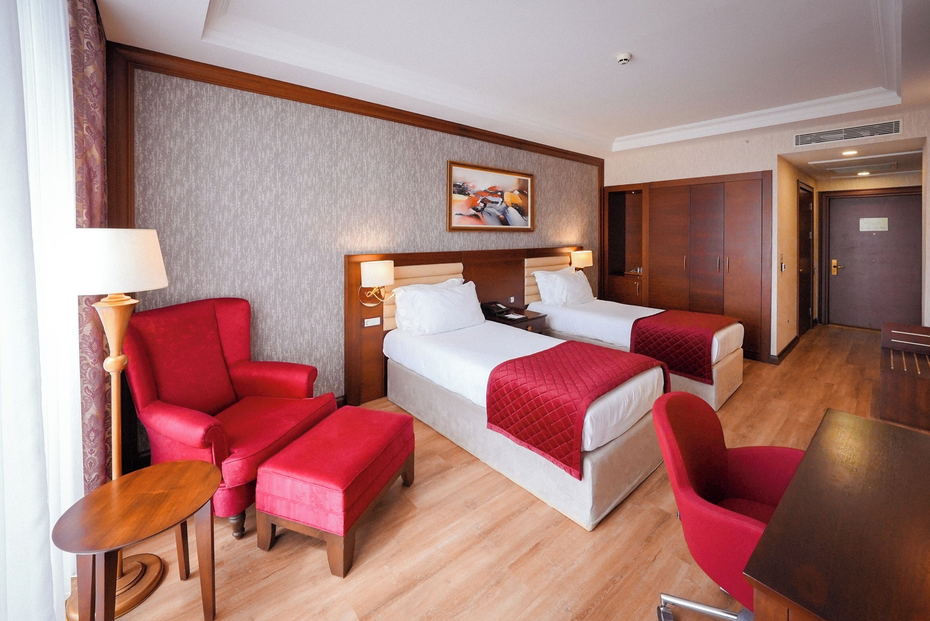 Habitación de hotel con dos camas, un sillón rojo, una mesita y un cuadro en la pared.