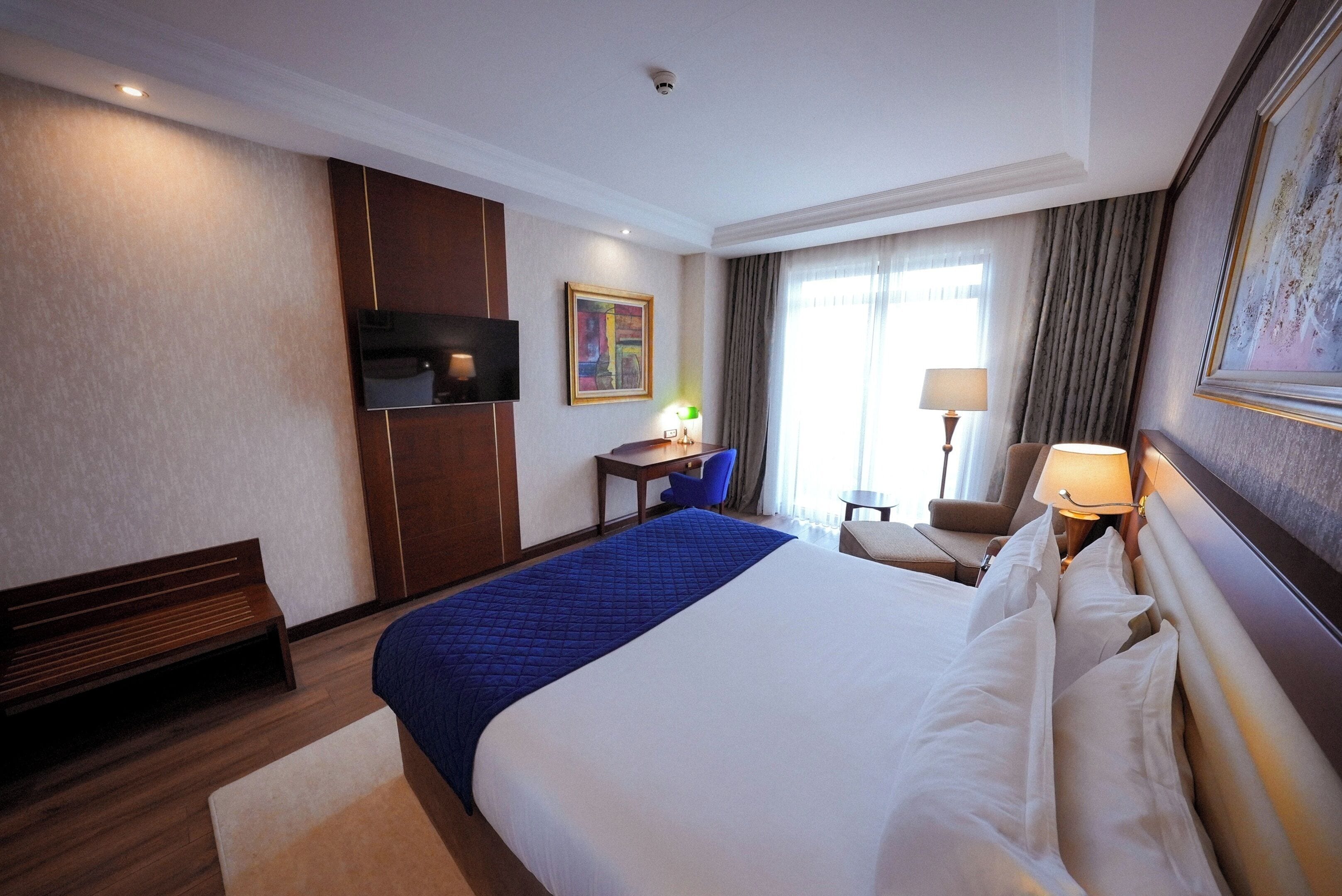 Habitación de hotel con una cama grande, un escritorio, una silla, un televisor y una ventana con cortinas.