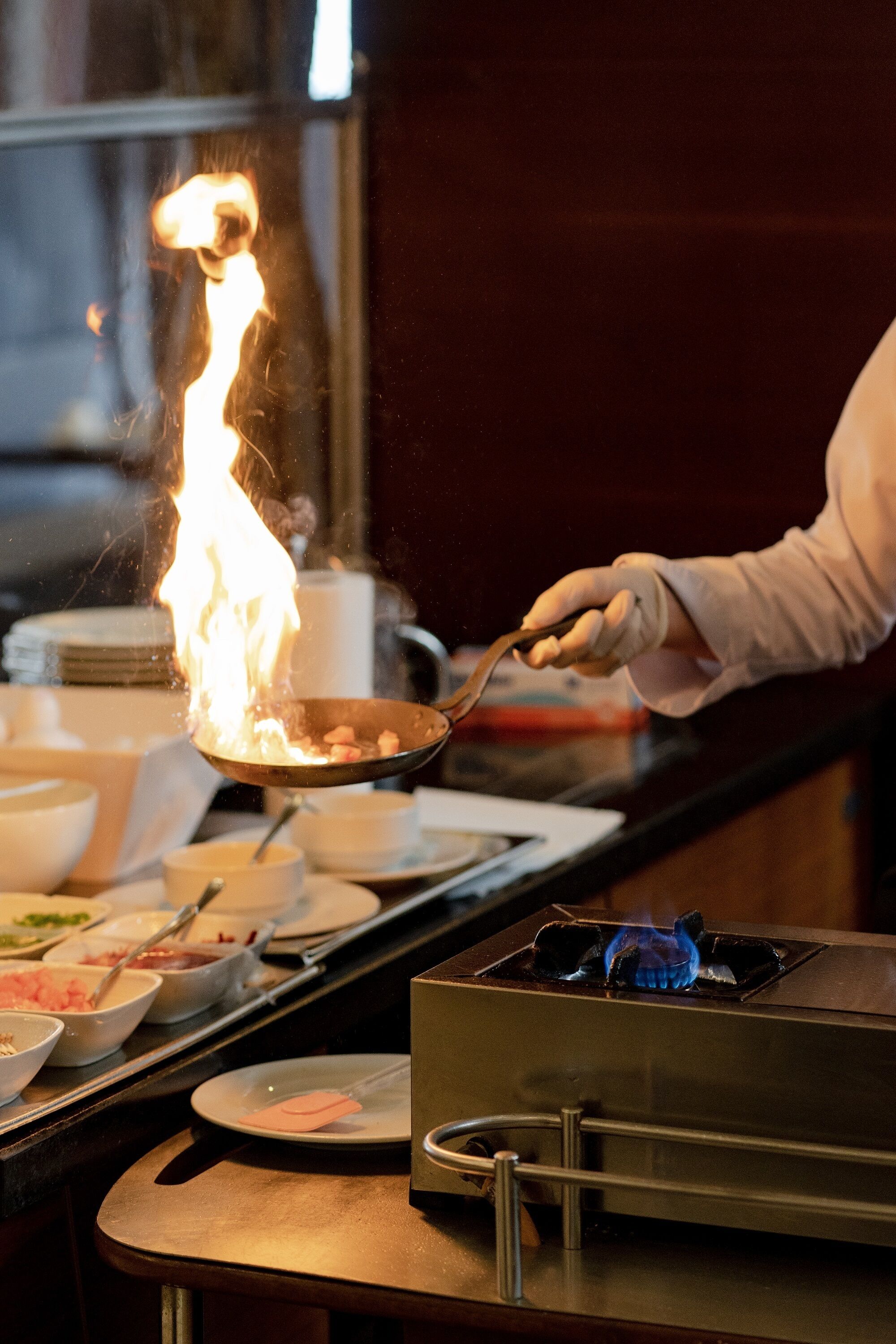 A person cooking with a flame, a stove, and various cooking utensils and dishes on a counter.