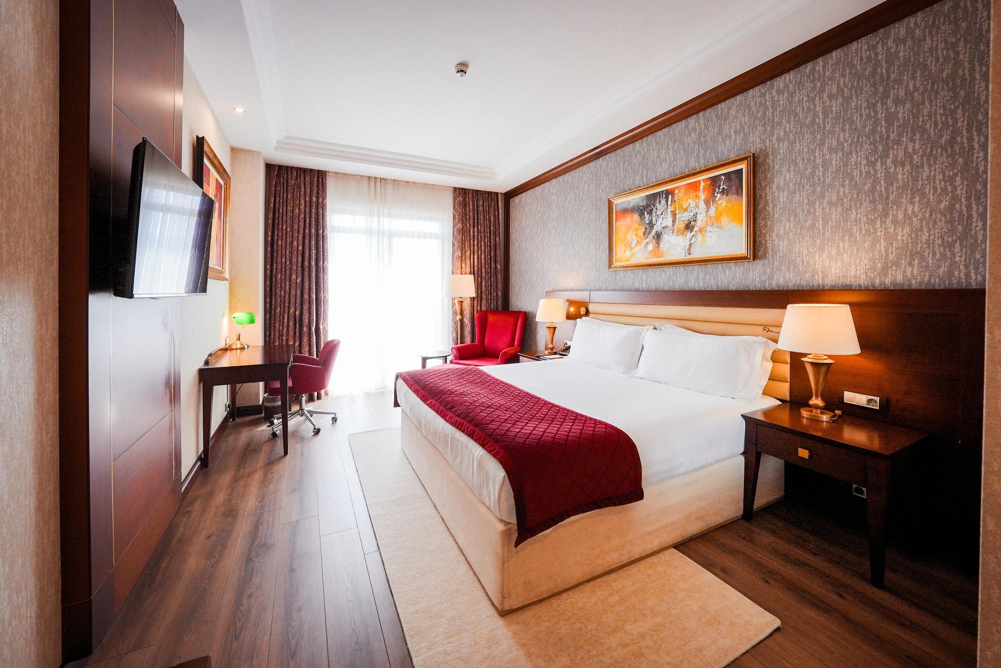 Een hotelkamer met een groot bed, een bureau, een stoel, een televisie en een schilderij aan de muur.