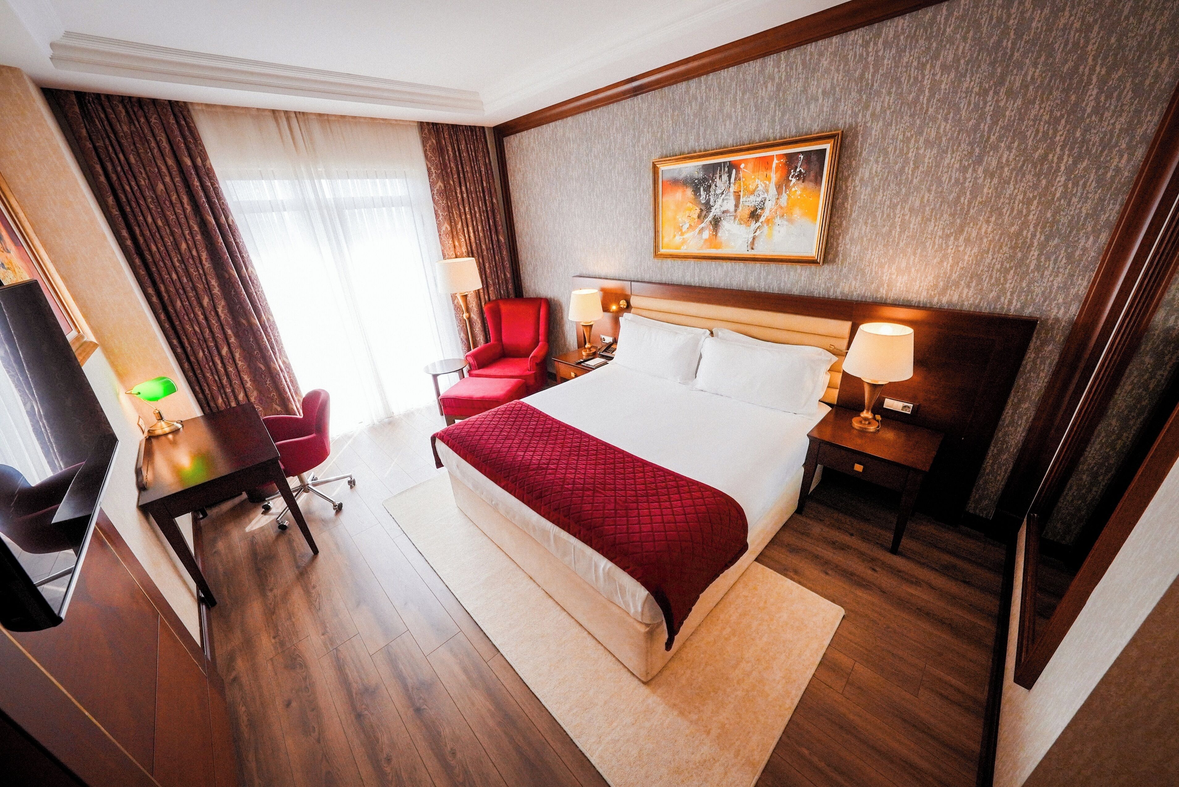 Una habitación de hotel con una cama, un escritorio, una silla, un televisor y un cuadro en la pared.