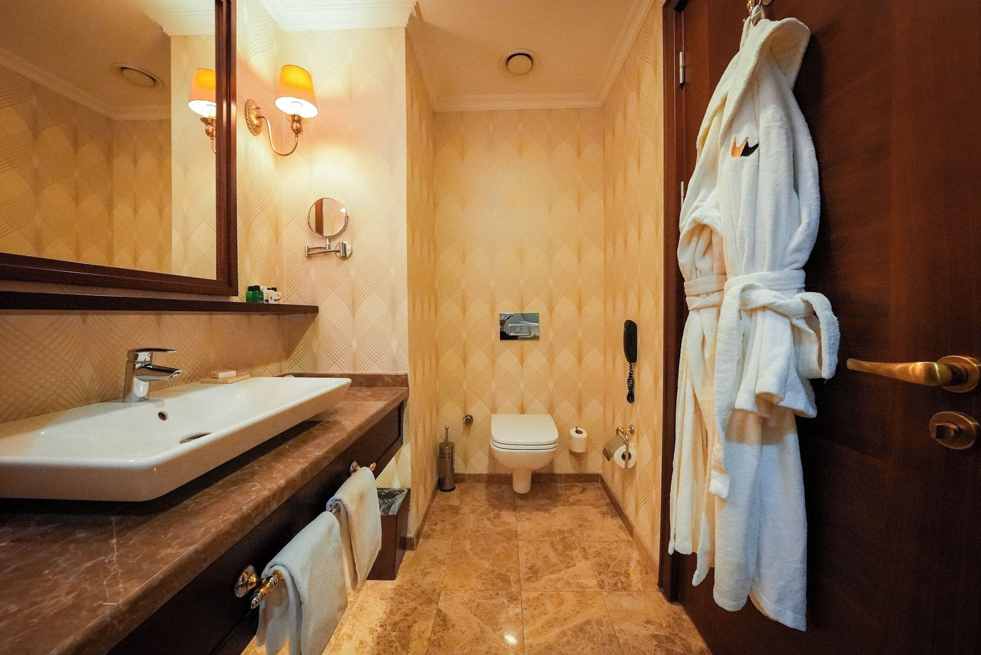 A bathroom with a sink, toilet, and a robe hanging on the door.