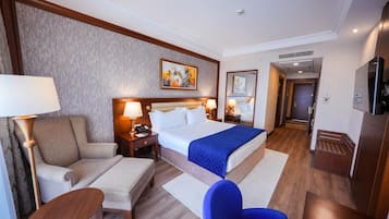 A hotel room with a bed, two bedside tables, a chair, a desk, a TV, and a door leading to the bathroom.