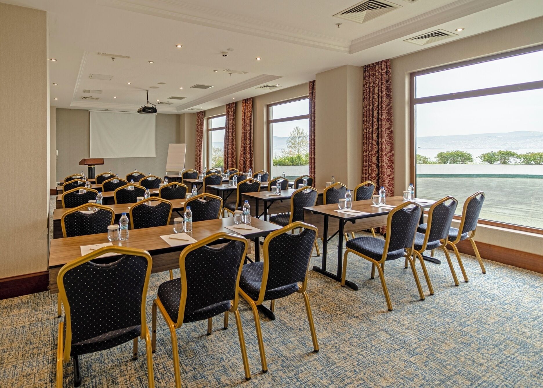 A conference room with tables and chairs, a projector screen, and a view of the water.