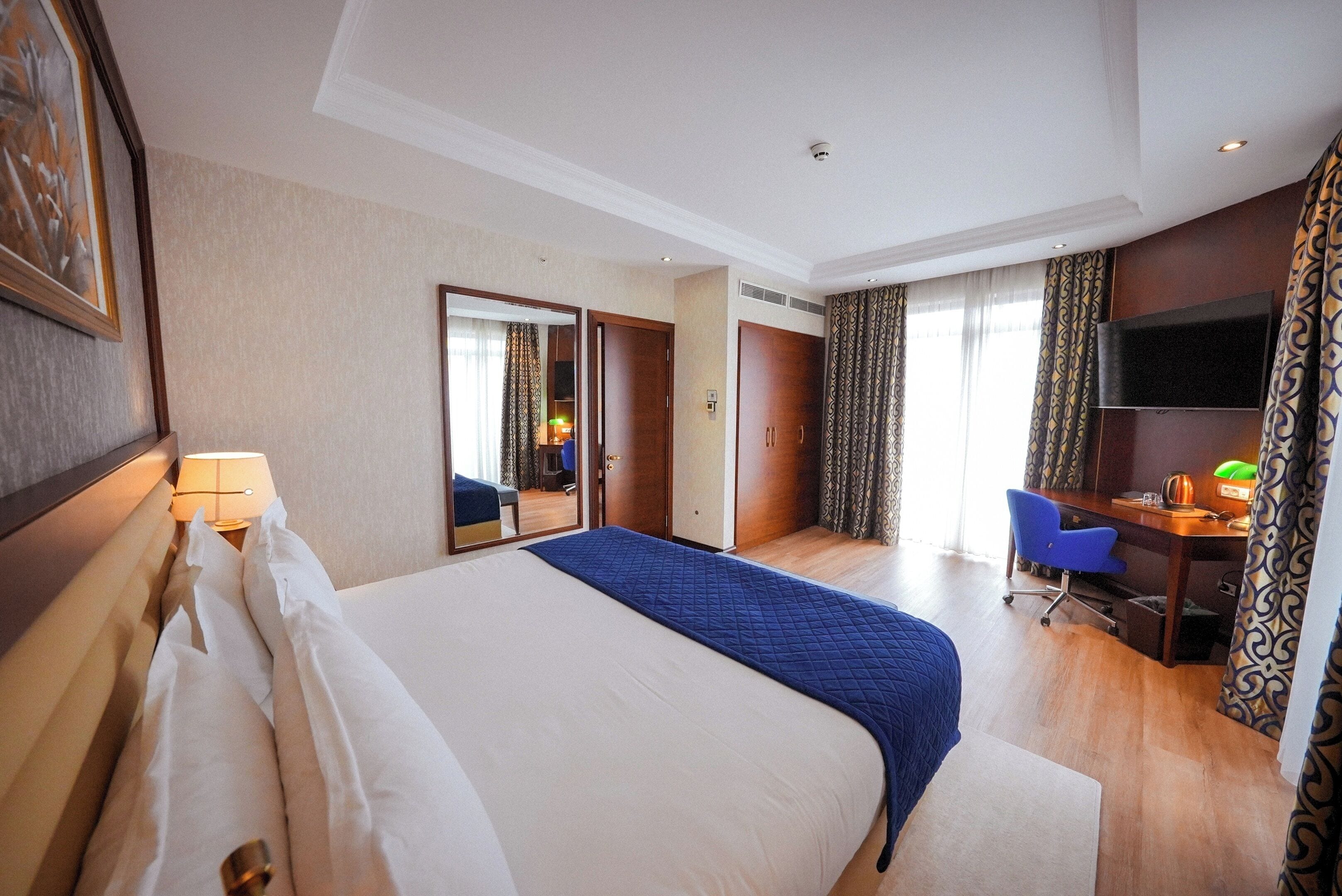 A hotel room with a large bed, a desk, a chair, a TV, and a mirror.