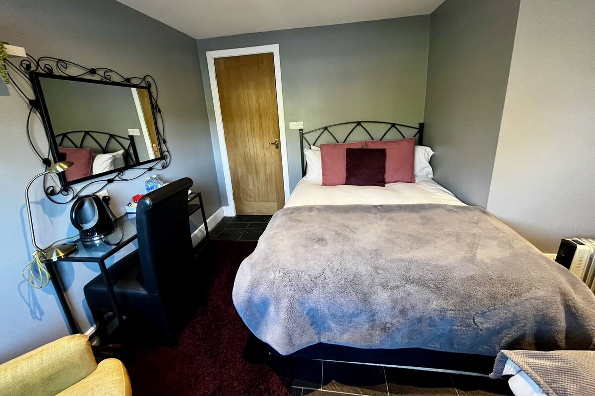 A bedroom with a bed, a desk, a chair, a mirror, and a door.