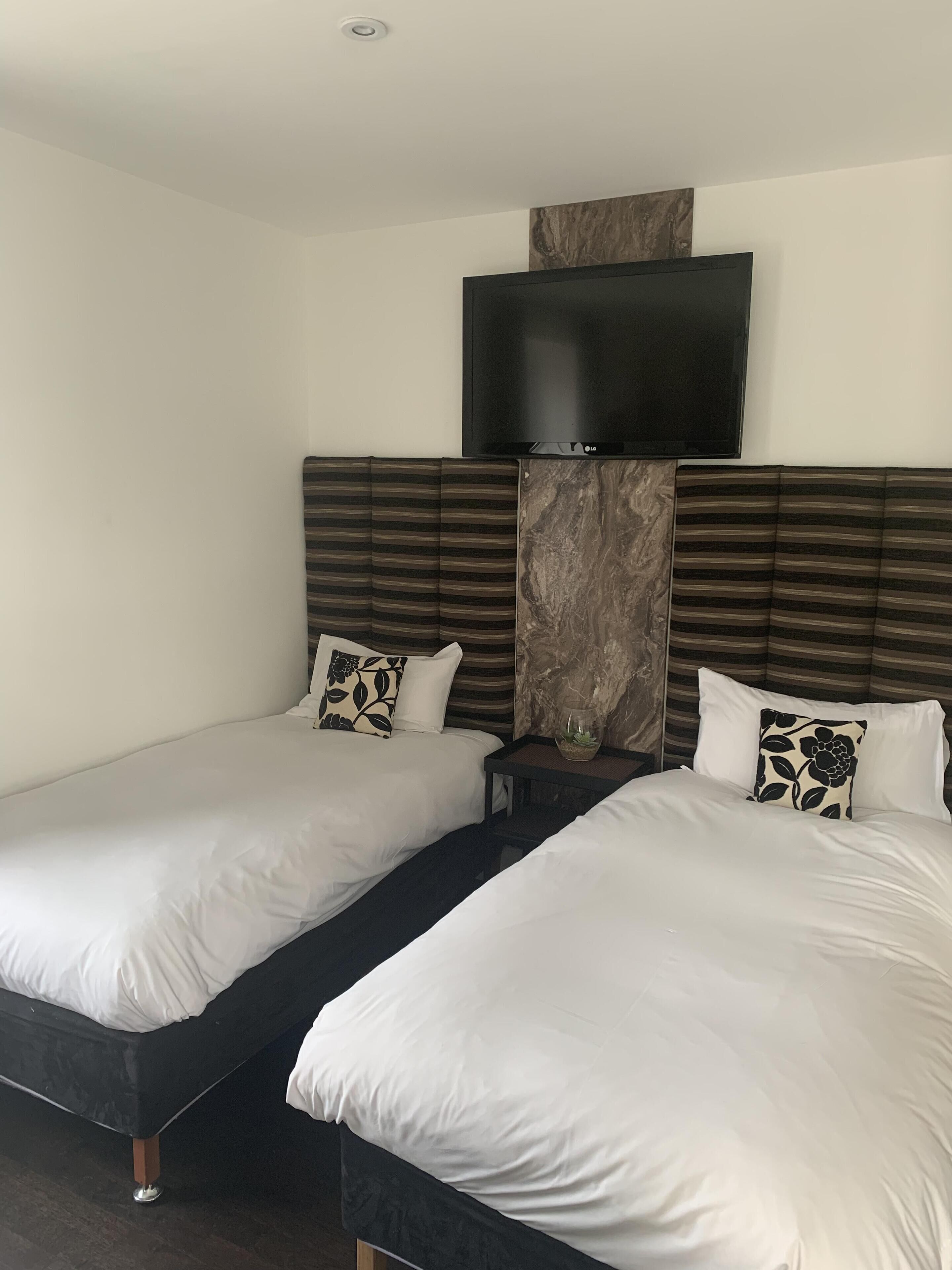A hotel room with two single beds, a flat-screen TV mounted above the beds, and a marble accent wall.