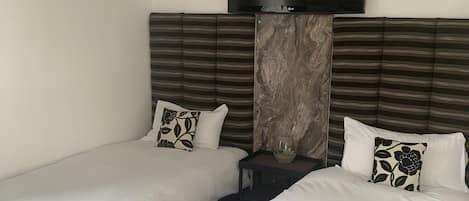 A hotel room with two single beds, a flat-screen TV mounted above the beds, and a marble accent wall.
