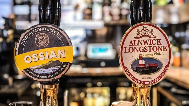 Dos grifos de cerveza con las etiquetas 'Ossian' y 'Alnwick Longstone' en un bar.