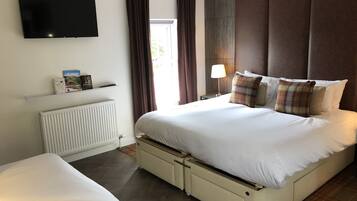 Une chambre d’hôtel comprenant un lit, une télévision, une table de chevet avec une lampe, une fenêtre avec des rideaux et un radiateur.