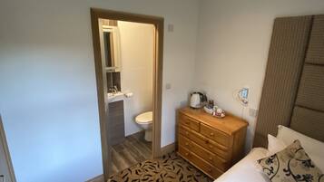 Habitación de hotel con cama, cómoda de madera, baño con inodoro y lavabo, y alfombra estampada.