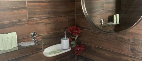 A modern bathroom with a wooden wall, a white sink, a mirror, a glass shelf with toiletries, and a red flower.