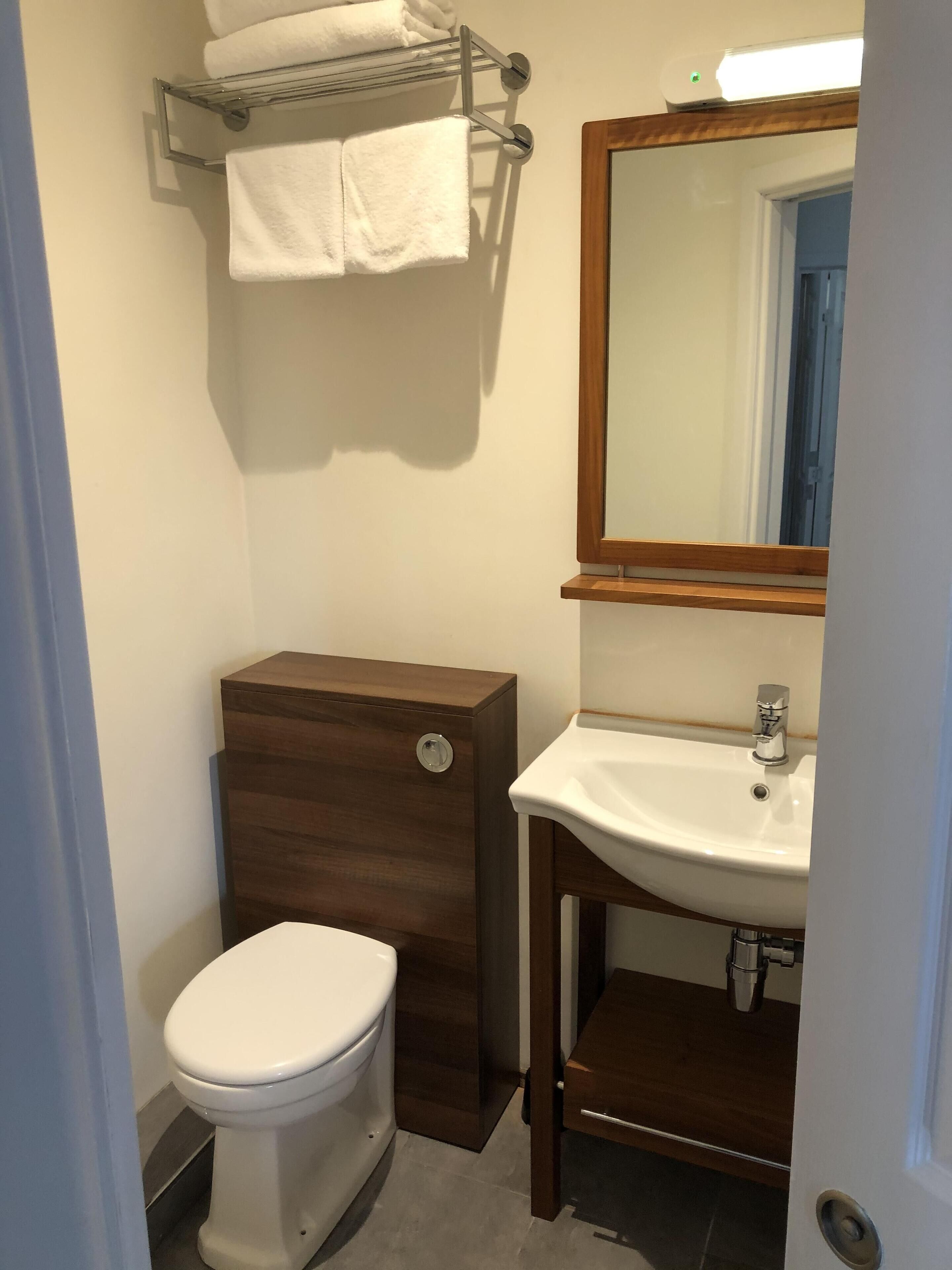 A compact bathroom with a toilet, a wooden vanity with a sink, and a towel rack above the toilet.