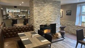 Un rincón de estar acogedor con pared de piedra, chimenea, asientos de cuero y un bar al fondo.