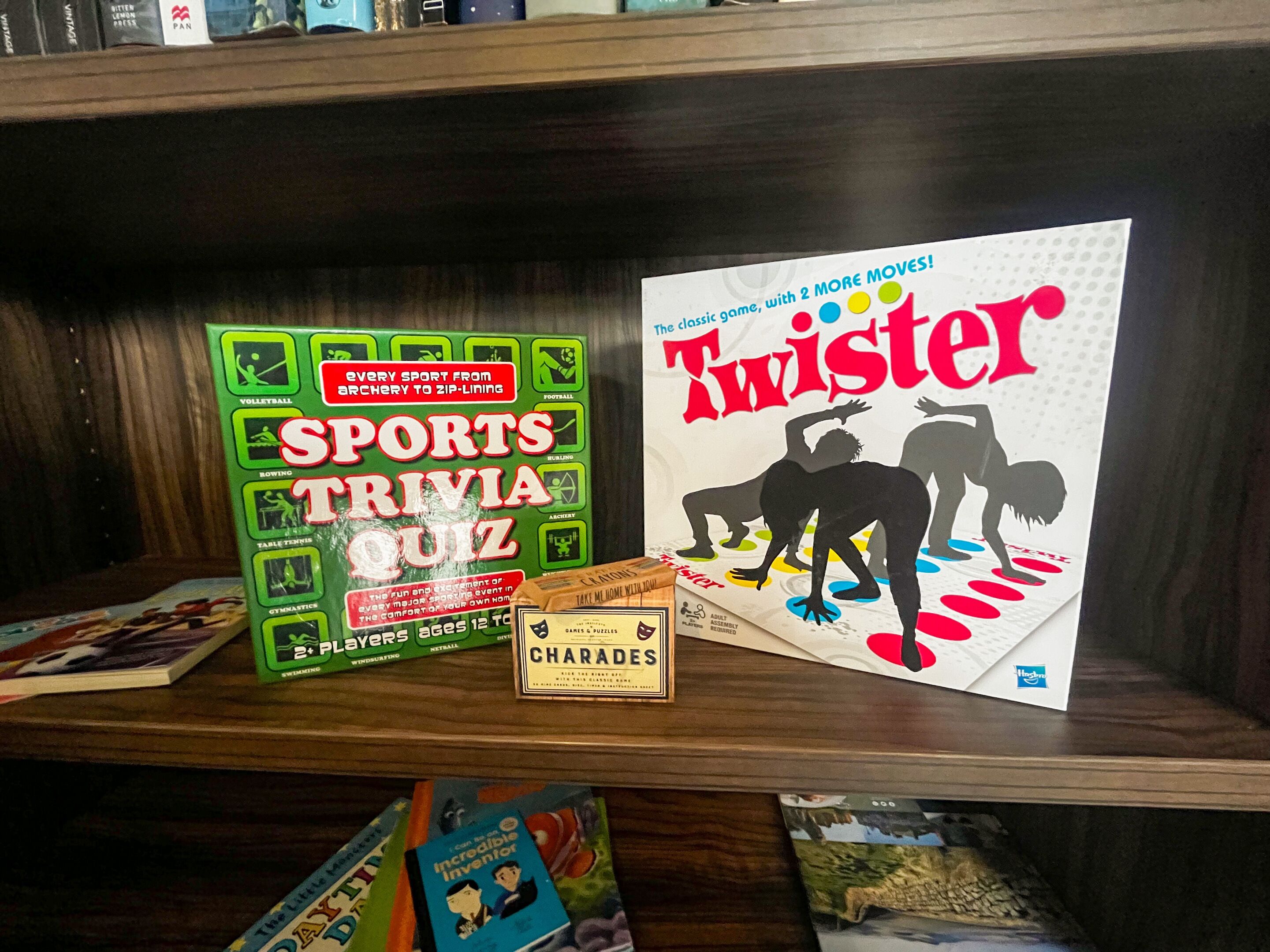 Una estantería con libros y juegos, incluyendo un 'Sports Trivia Quiz' y 'Twister'.