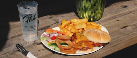 Un plato de comida con una hamburguesa, papas fritas, aros de cebolla, un vaso de agua y una servilleta sobre una mesa de madera.