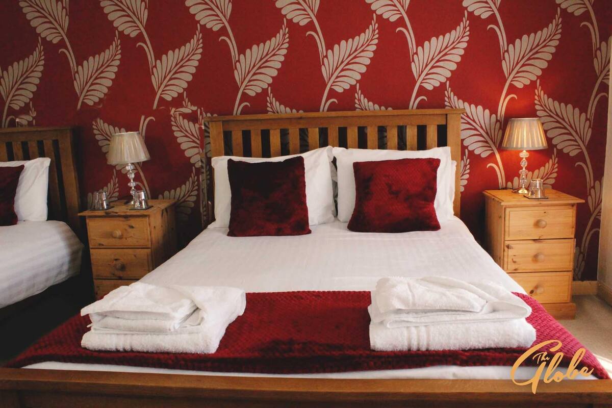A double bed with two red pillows, a wooden headboard, two bedside tables with lamps, and a red throw blanket.