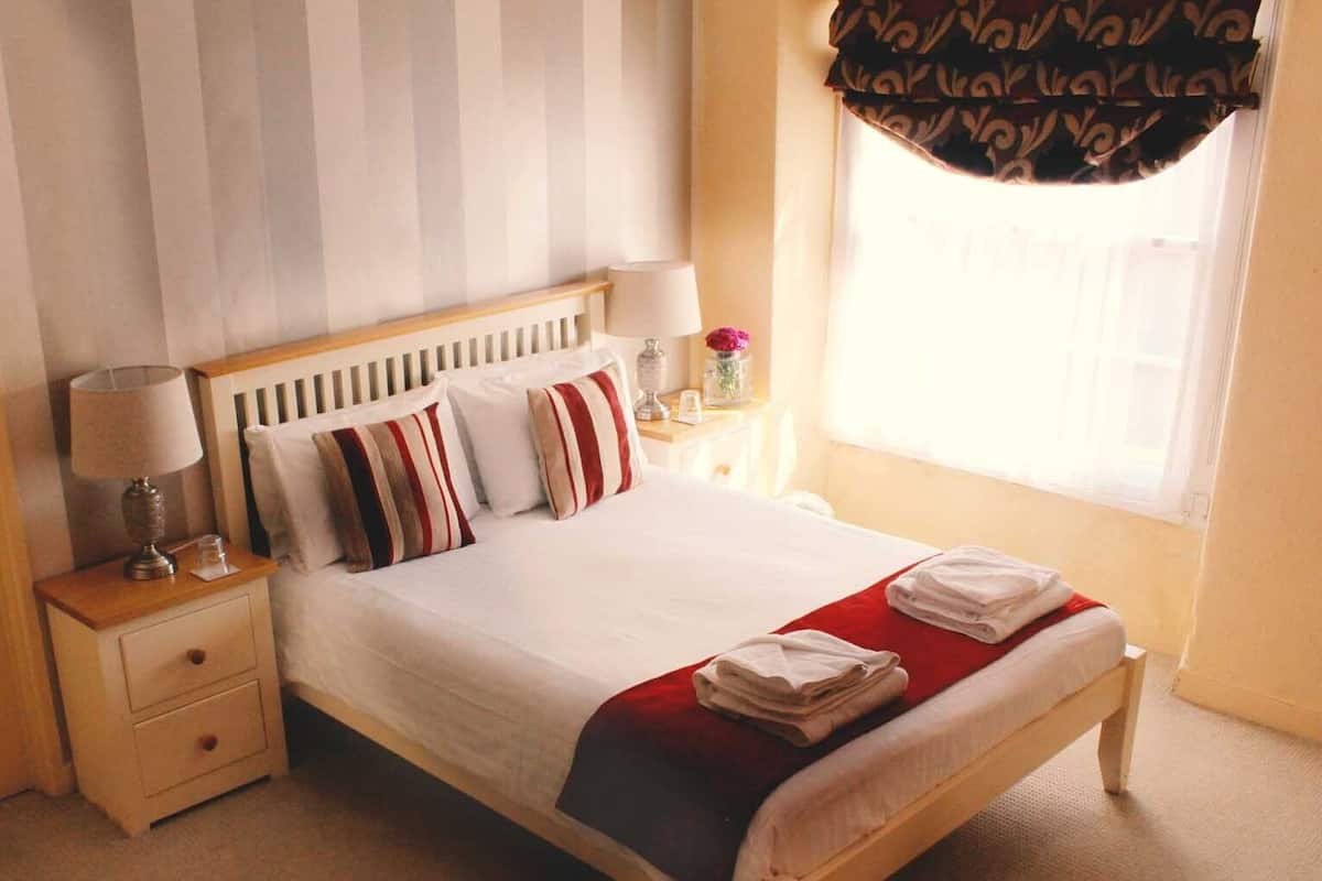 A neatly made bed with striped pillows, a bedside table with a lamp, and a window with curtains.