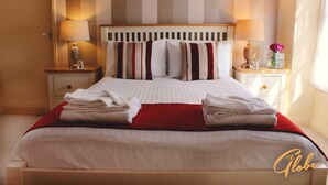 A neatly made bed with striped pillows, two bedside tables with lamps, and a red throw blanket. - The Globe Inn (Tiverton)