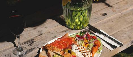 A wooden table with a plate of food, a glass of red wine, and a vase with yellow flowers.