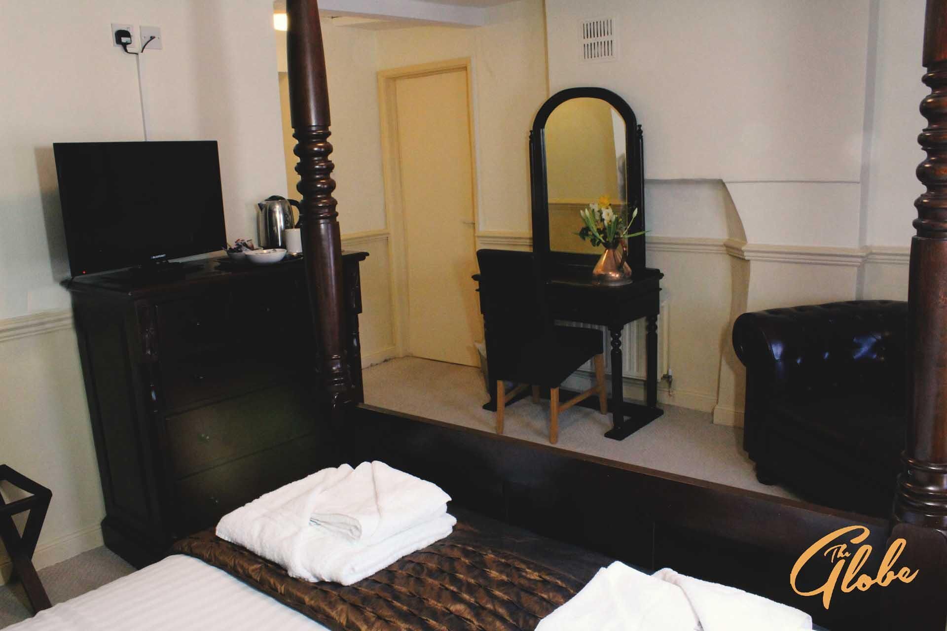 A hotel room with a bed, a dresser, a mirror, a television, and a small table with a vase of flowers.