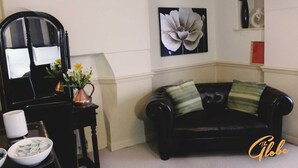 A living room with a black leather sofa, a coffee table with a vase of flowers, a black armchair, and a painting on the wall. - The Globe Inn (Tiverton)