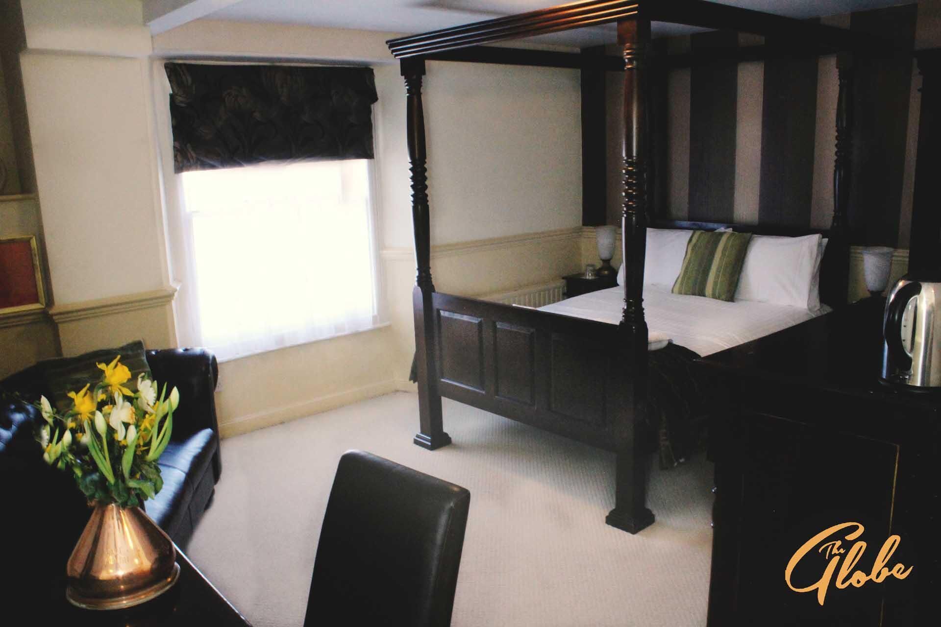 A four-poster bed with a nightstand and a vase of flowers.