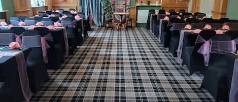 Un salón de banquetes con suelo a cuadros, mesas adornadas con cintas rosas y globos.