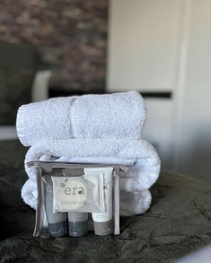A bathroom with a towel rack holding a white towel and a small shelf with toiletries including a bottle labeled "era natural soap".