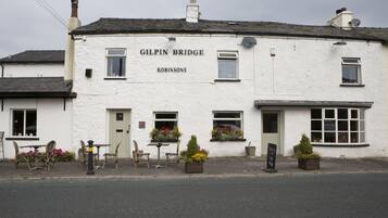 A white building with the sign "Gilpin Bridge" and "Robinsons" on it. There are outdoor tables and chairs, and flower pots on the sidewalk.