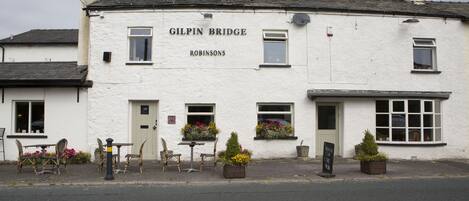Ein weißes Gebäude mit der Beschilderung "Gilpin Bridge" und "Robinsons". Draußen stehen Tische und Stühle, und auf dem Bürgersteig befinden sich Blumentöpfe.