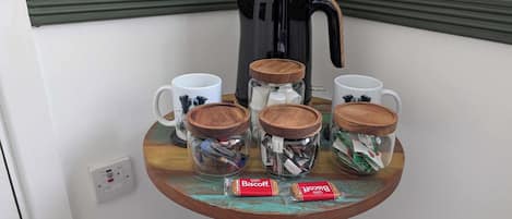 A small table with four glass jars containing snacks, two white mugs, and a coffee maker.