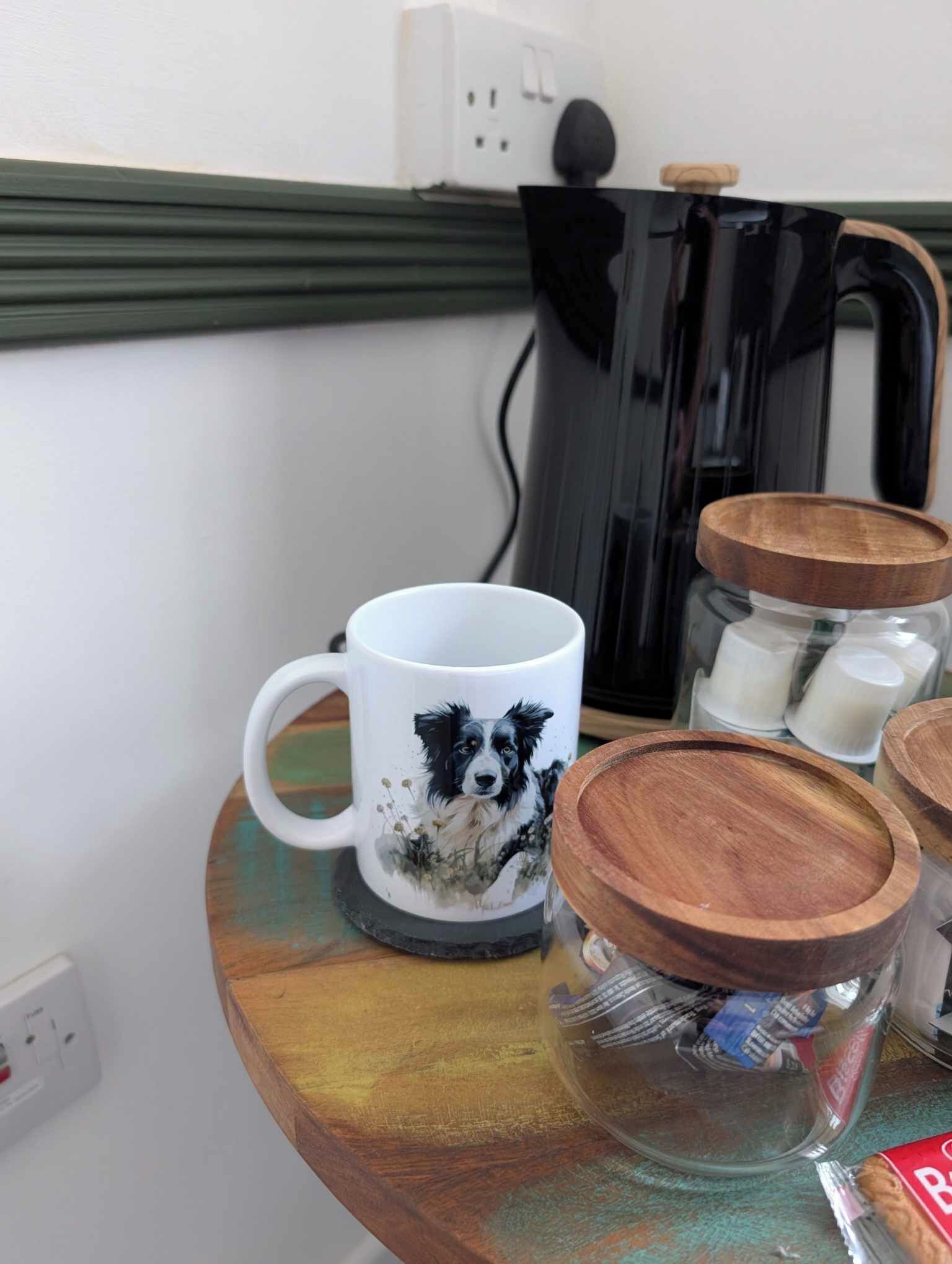 A mug with a dog design, wooden jars, and a coffee maker on a table.